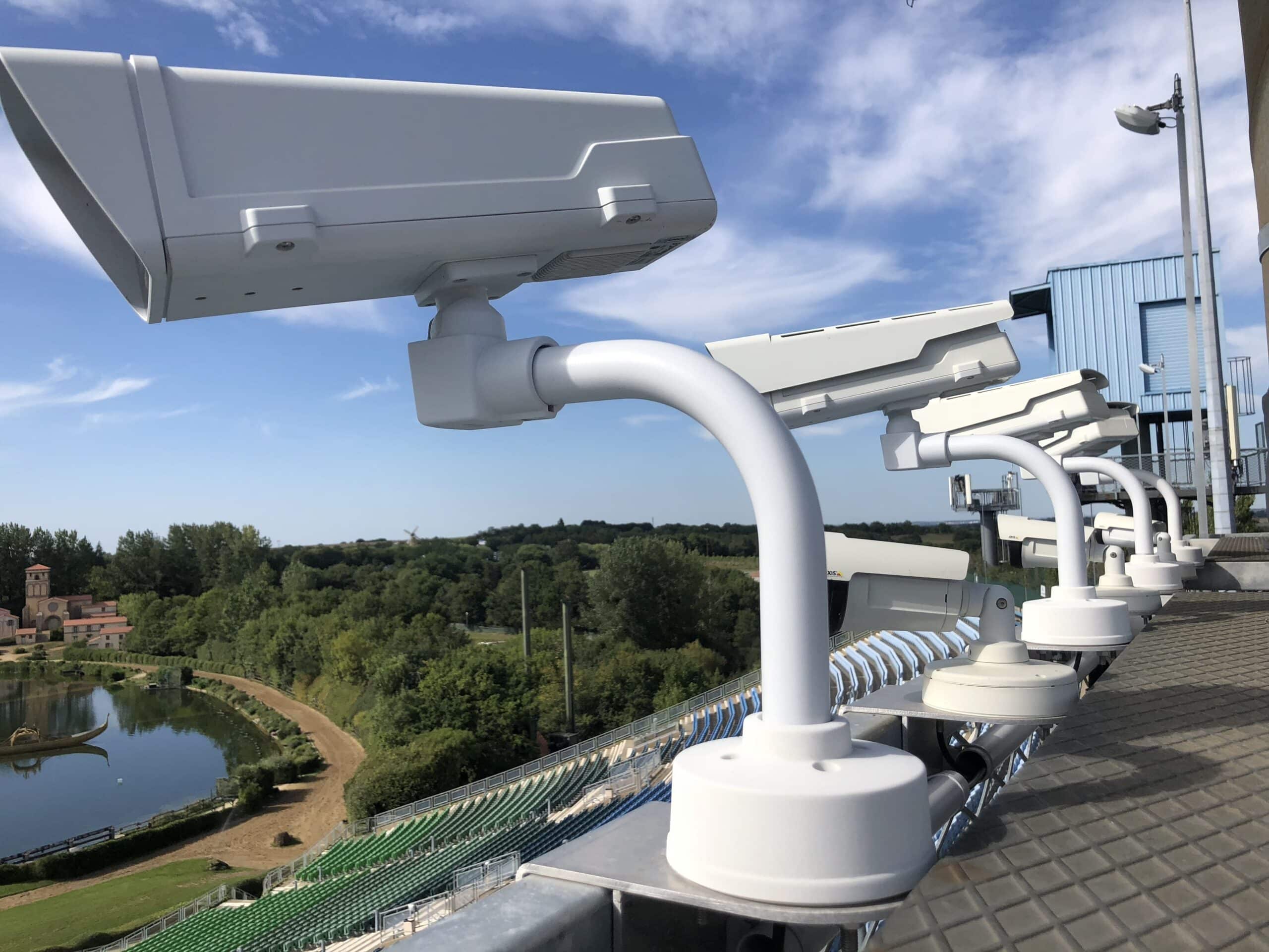 Rangée de caméras de vidéosurveillance professionnelles installées en hauteur sur un stade avec vue panoramique sur un parc de loisirs et un plan d'eau